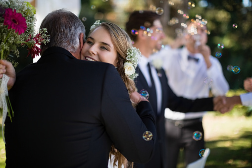 Father embracing his daughter in park during wedding