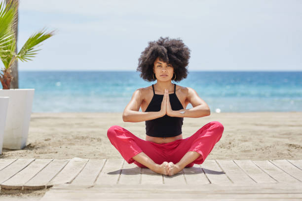 istock Young afro american woman meditating on beach 829719908