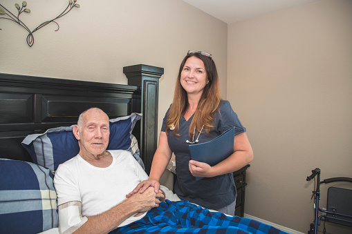 A stock photo of a Hospice nurse helping an elderly man with Parkinson's Disease and Cancer. The man is receiving palliative hospice care at home.