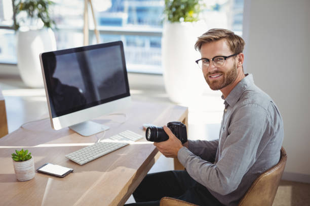 Portrait of smiling executive holding digital camera at desk in office