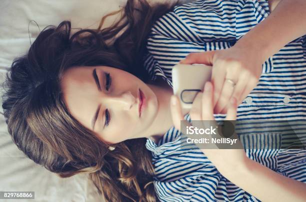 Closeup Of Pretty Teenage Girl Lying In Bed An Looking At Her Mobile Phone Stock Photo - Download Image Now