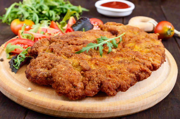 a large viennese schnitzel  and tomato salad on a cutting board on a dark wooden background. close up - viennese schnitzel imagens e fotografias de stock