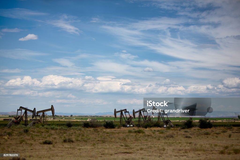 Fracking Pumpjacks in the Oil Field Pumpjacks on the horizon underneath a partly cloudy beautiful sky.  These pieces of equipment are crucial to oil field and fracking operations Landscape - Scenery Stock Photo