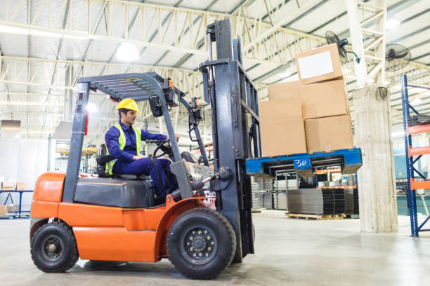 worker driving a forklift in warehouse Worker driving a forklift loader in warehouse with load. Operator in uniform moving cardboard boxes by forklift loader. forklift truck stock pictures, royalty-free photos & images