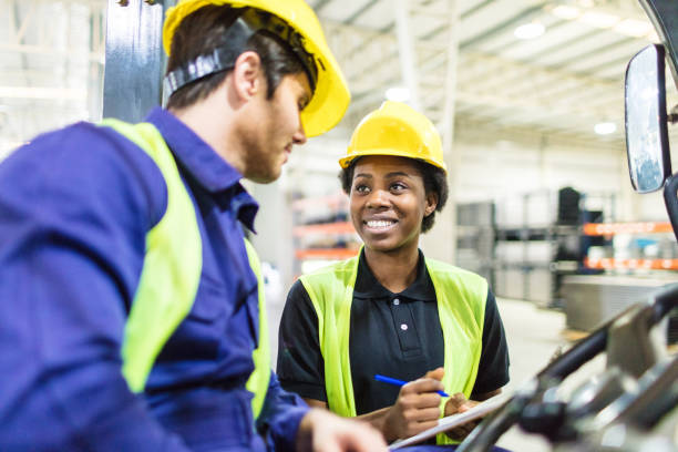 Warehouse workers discussing shipping schedule Woman talking to forklift truck operator in warehouse. Warehouse workers discussing shipping schedule. manufacturing occupation stock pictures, royalty-free photos & images