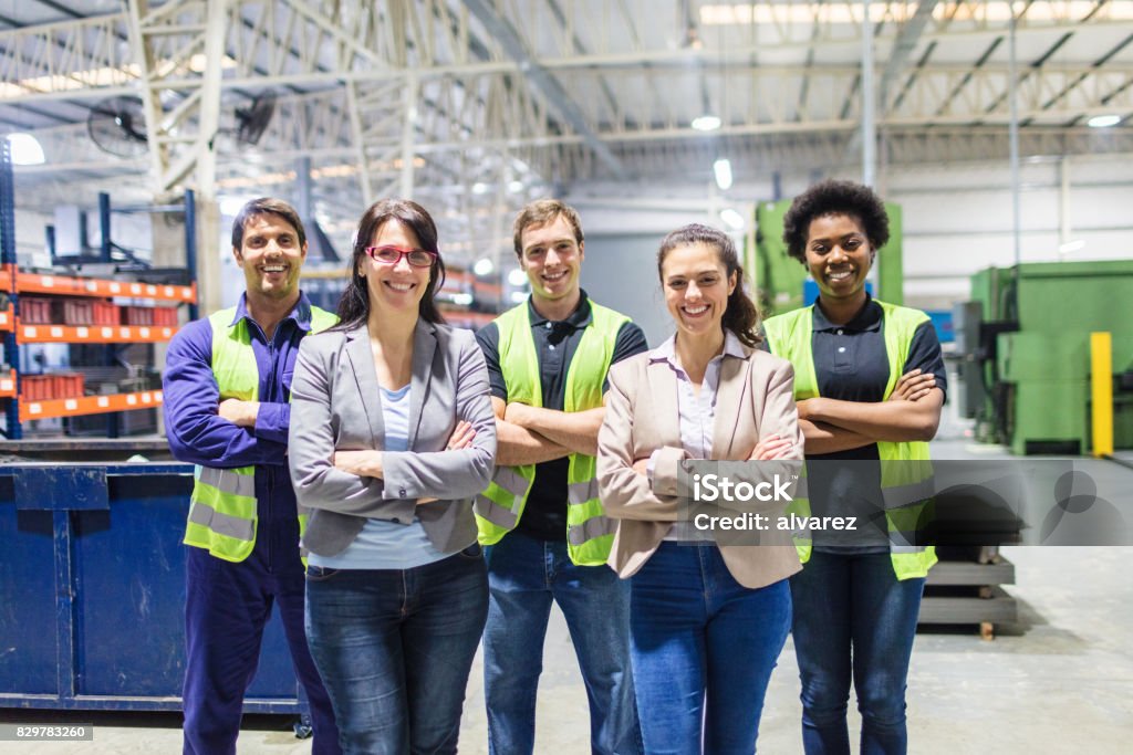 Portrait of staff at distribution warehouse Group portrait of staff at distribution warehouse. Warehouse team standing with arms crossed in factory. Teamwork Stock Photo