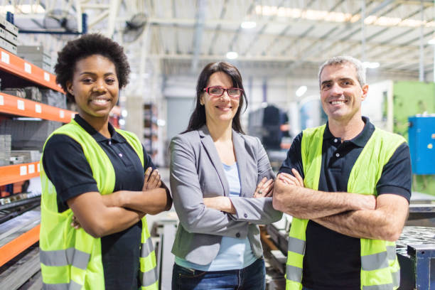 Warehouse manager and workers standing together Portrait of warehouse manager and workers standing together with arms crossed in factory. Warehouse team looking at camera and smiling. manufacturing occupation photos stock pictures, royalty-free photos & images