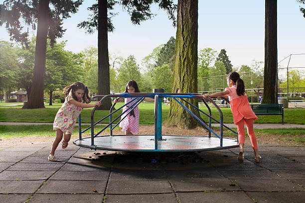 kids on carousal in playground 3 girls pushing carousal in playground playground stock pictures, royalty-free photos & images
