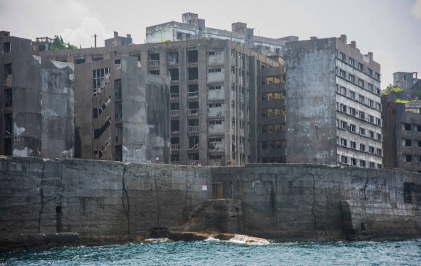 Battleship Island (Gunkanjima, Hashima, Gunkanjima, Gunkanjima, Gunkanjima) Hashima Island (端島 or simply Hashima — -shima is a Japanese suffix for island), commonly called Gunkanjima (軍艦島; meaning Battleship Island), is an abandoned island lying about 15 kilometers (9 miles) from the city of Nagasaki, in southern Japan. It is one of 505 uninhabited islands in Nagasaki Prefecture. The island's most notable features are its abandoned concrete buildings, undisturbed except by nature, and the surrounding sea wall. While the island is a symbol of the rapid industrialization of Japan, it is also a reminder of its dark history as a site of forced labor prior to and during the Second World War. sites of japans meiji industrial revolution photos stock pictures, royalty-free photos & images