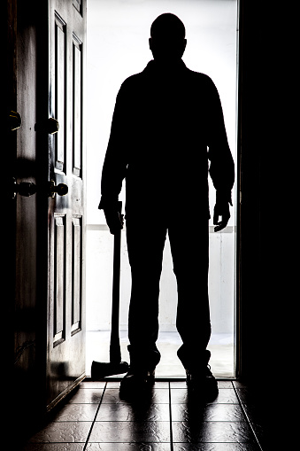 Intruder standing at doorway threshold, in silhouette with axe