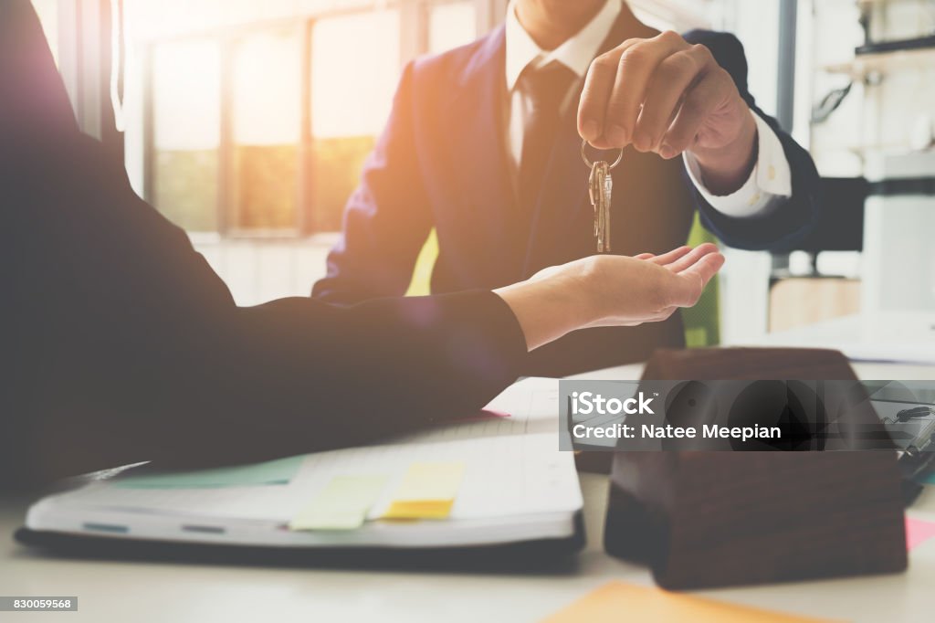 estate agent giving house keys to man and sign agreement in office estate agent giving house keys to woman and sign agreement in office Closing Stock Photo