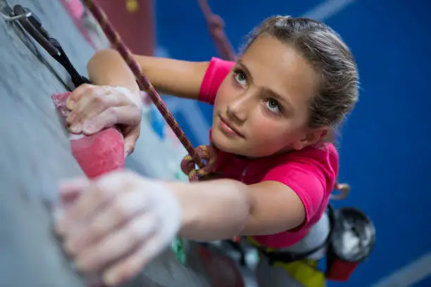 Determined teenage girl practicing rock climbing in fitness studio