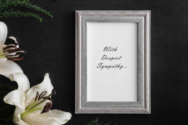White blank condolence card with text in the frame. Lily flowers on the dark background.