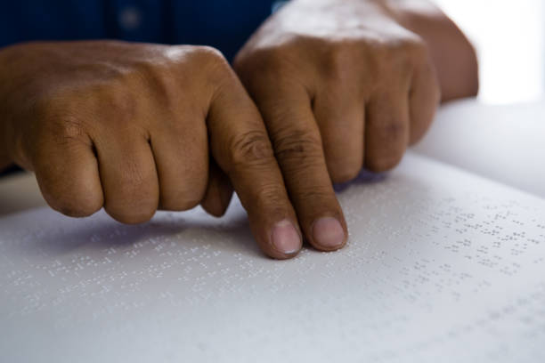 istock Cropped fingers on senior man reading braille book at table 830196162