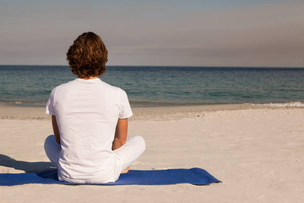 istock Rear view of man meditating at beach 830202788