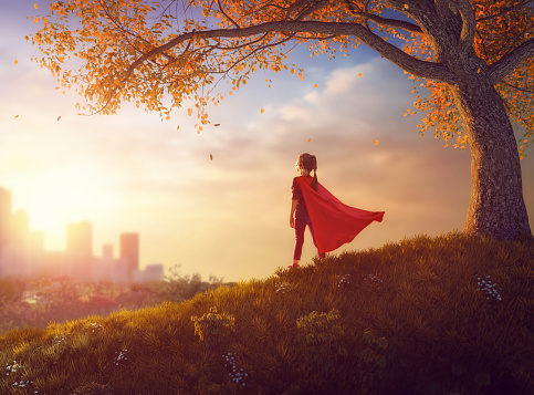 Little child is playing superhero. Kid on the background of autumn landscape. Girl power concept.