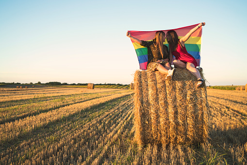 Lesbian couple with LGBT flag on a cropped field