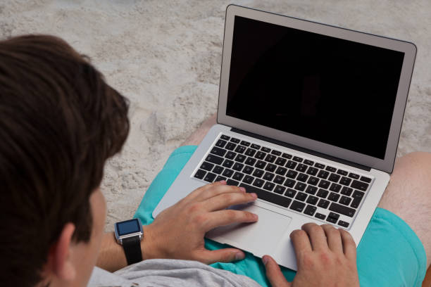 istock High angle view of man using laptop at beach 830245826