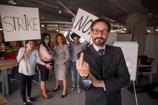 istock Happy director in loft office showing long finger to camera, striking workers behind him. 830246452