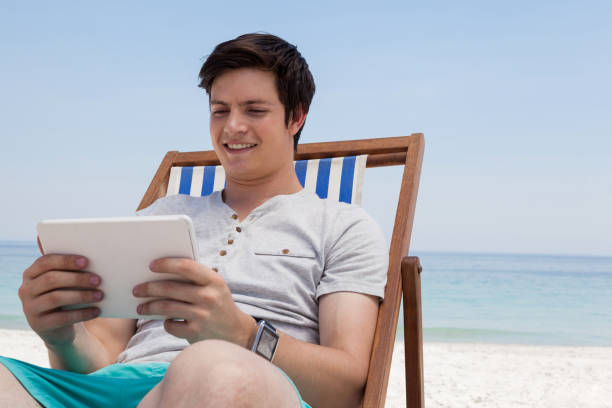 istock Man sitting on sunlounger and using digital tablet on the beach 830247938