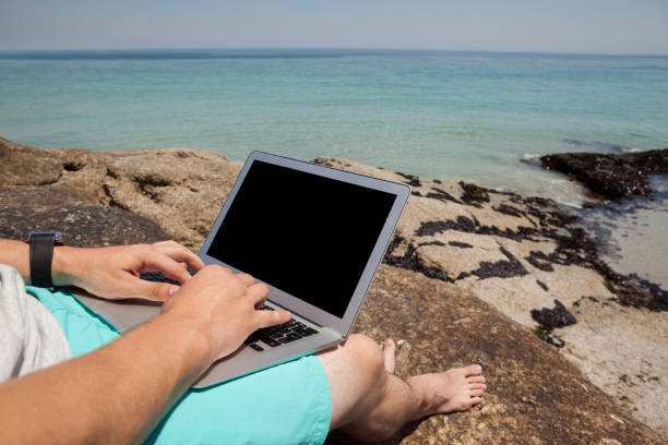 istock Man sitting on the rocks and using laptop at the sea coast 830253364
