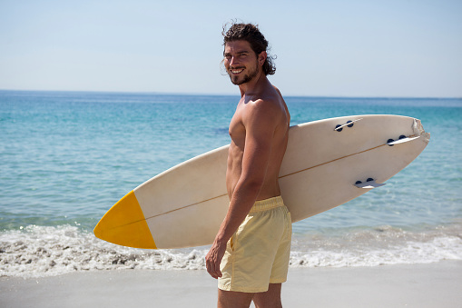 Portrait of smiling surfer with surfboard standing at beach coast