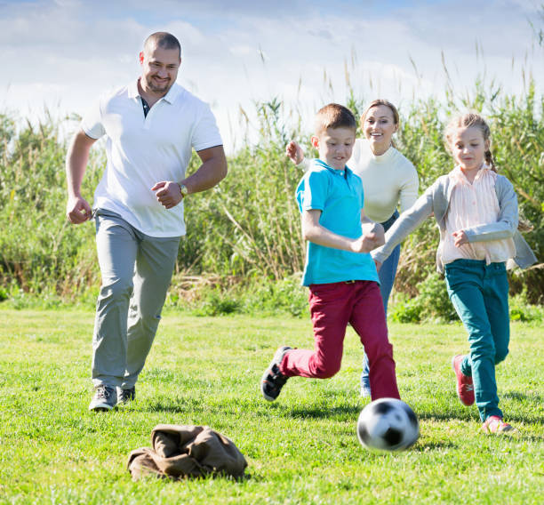 istock Mother and father with two kids  running after  ball 830284916