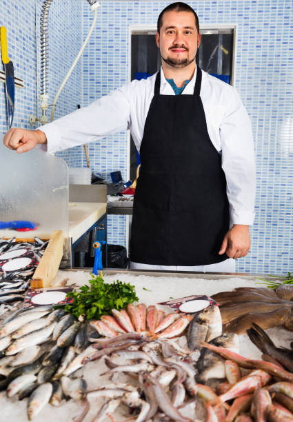 istock Seller in black apron shows fish counter 830291452