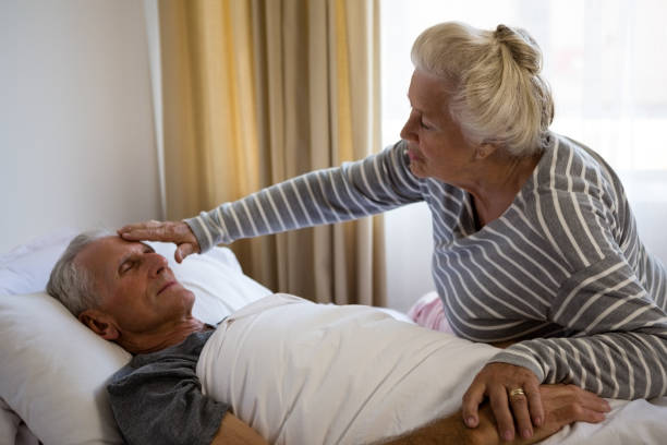 istock Senior woman sitting by husband sleeping on bed 830299048