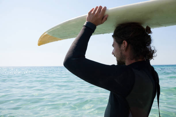 istock Surfer in wetsuit carrying surfboard over head at beach coast 830299282