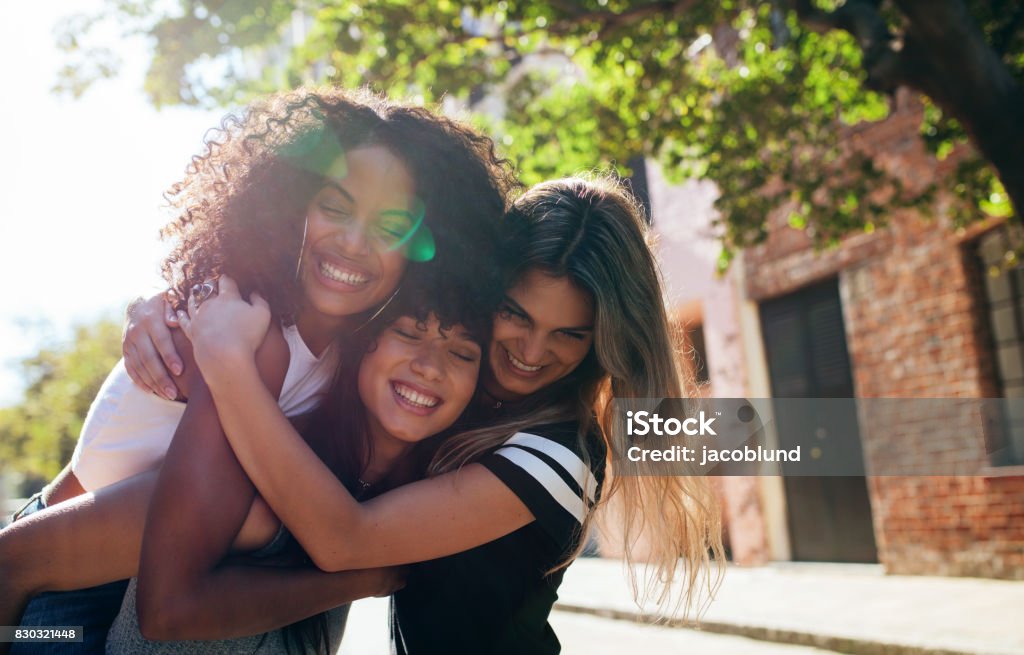 Group of female friends enjoying outdoors on city street Three happy young women embracing each other on city street and smiling. Group of friends enjoying outdoors on city street. Friendship Stock Photo