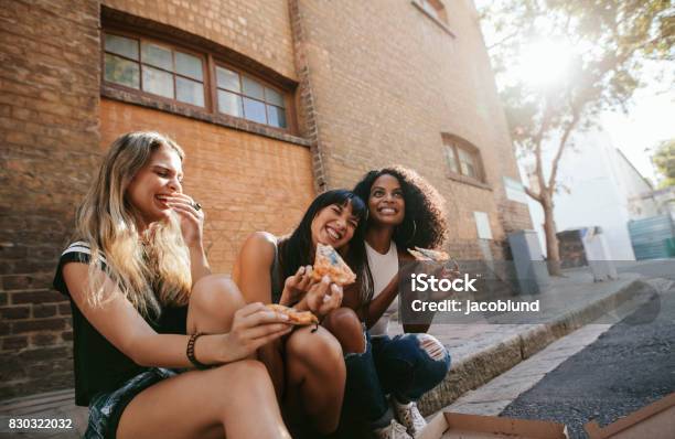 Foto de Belas Garotas Sentado Ao Ar Livre À Beira Da Estrada Comendo Pizza e mais fotos de stock de Pizza