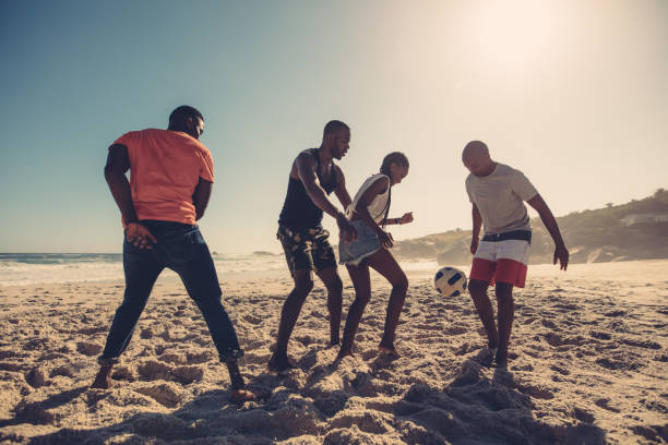 amigos disfrutando de un partido de fútbol en la playa - beach football fotografías e imágenes de stock