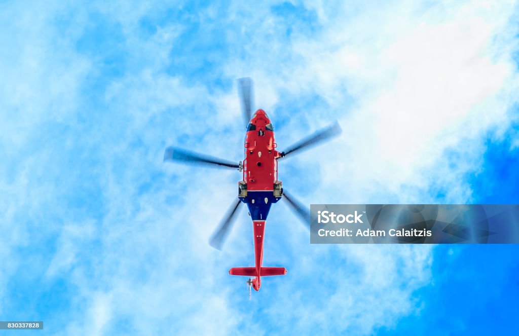 Get to the chopper Looking up underneath a blue and red helicopter against a blue sky with light clouds Helicopter Stock Photo