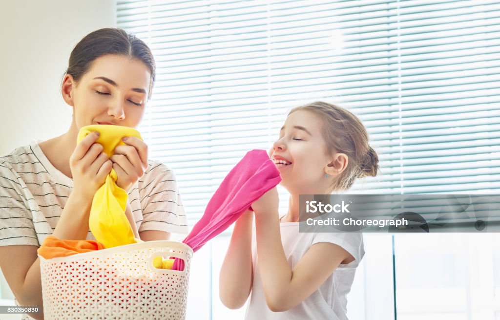 family doing laundry at home Beautiful young woman and child girl little helper are smelling clean clothes and smiling while doing laundry at home. Clothing Stock Photo