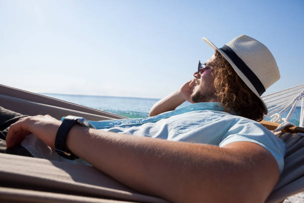 istock Man relaxing on hammock and talking on mobile phone on the beach 830358242