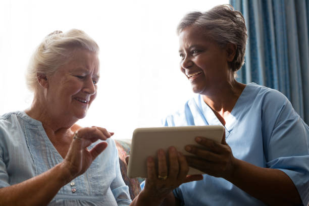 cheerful senior woman with doctor using digital tablet while sitting on sofa - digital tablet women enjoyment happiness imagens e fotografias de stock