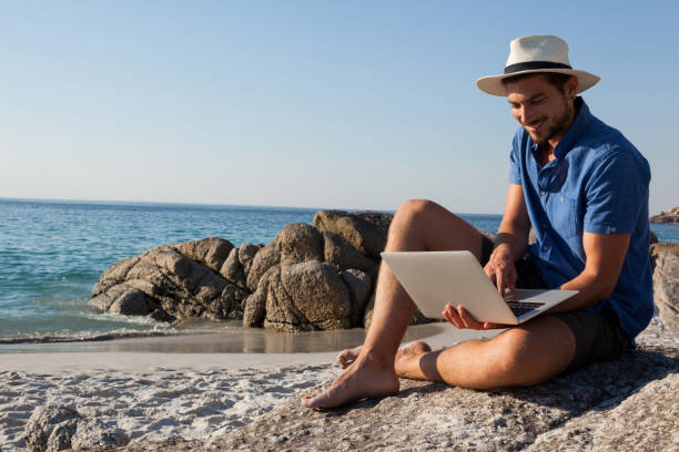 istock Man sitting on the rocks and using laptop on beach 830374220