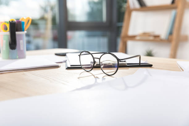 istock selective focus of round eyeglasses on workplace with papers and clipboard 830384902