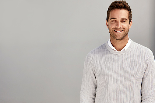Grey sweater guy smiling against grey background