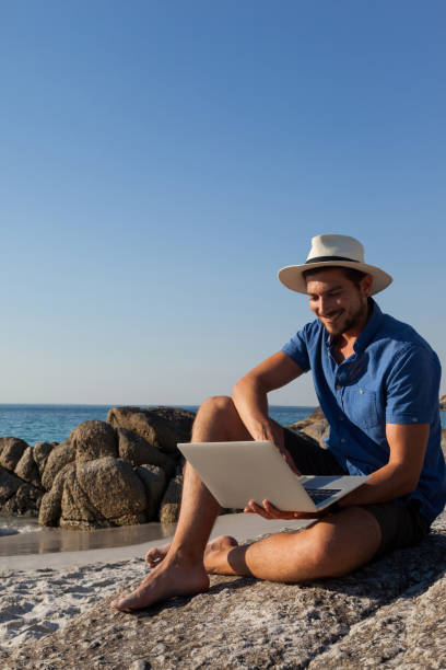 istock Man sitting on the rocks and using laptop on beach 830404324