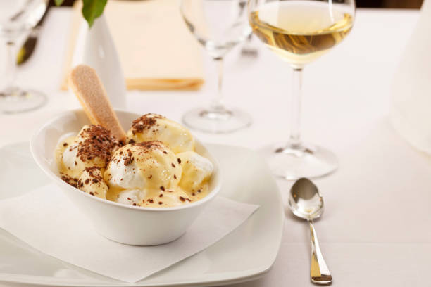 Clara de huevo con mousse de vainilla dispuesta en un plato, Copa de vino en el fondo, un postre tradicional en elegante entorno, enfoque selectivo con la luz suave - foto de stock