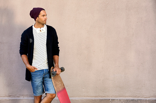 Dude in cool clothes holding skateboard, looking away