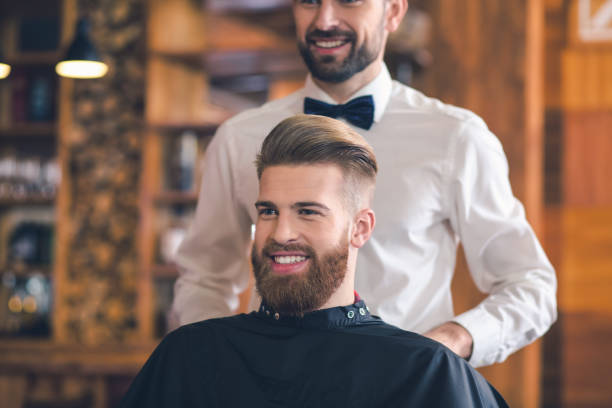 Young Man in Barbershop Hair Care Service Concept Young man sitting in a barbershop cheerful preparation for the haircut looking in mirror stock pictures, royalty-free photos & images