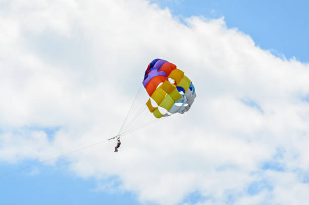 istock Colored parasail wing in the blue clouds sky, Parasailing also known as parascending or parakiting 830427098