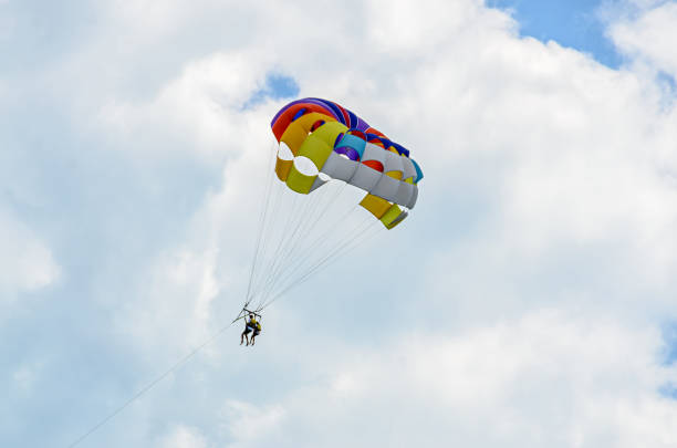 istock Colored parasail wing in the blue clouds sky, Parasailing also known as parascending or parakiting 830429124