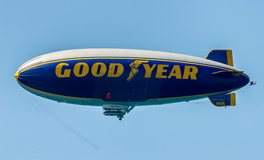 Famous Goodyear blimp, which has become an icon representing American automotive industry, delights beach goers by flying over California coastline during summer season. The picture was taken from Malibu beach in Southern California, when thousands of tourists and locals take to the beach.