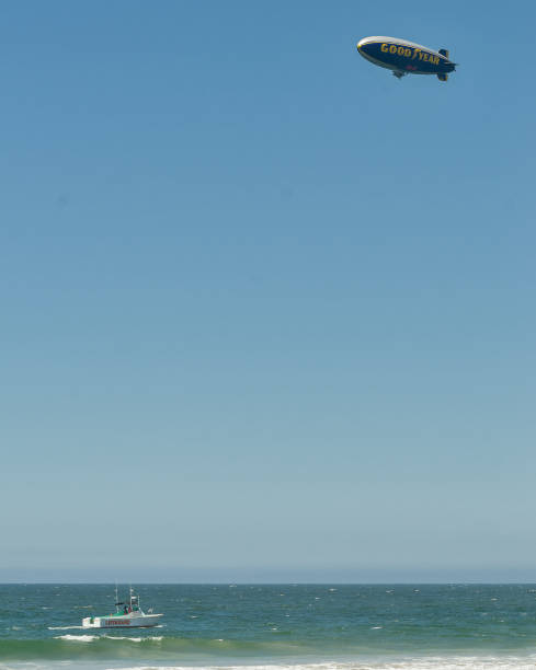 dirigeable goodyear sur le ciel et le bateau de garde-côtes patrouillant california beach - goodyear blimp photos et images de collection