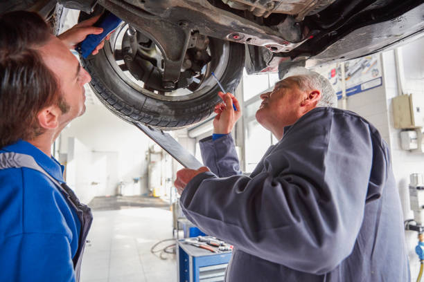 istock Mechanic And Male Trainee Working Underneath Car Together 830511690