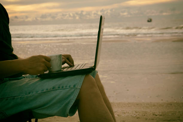 istock A man using laptop and holding a cup on the beach. 830594168
